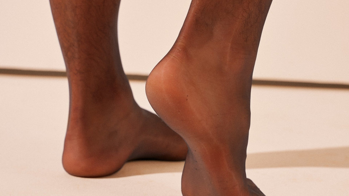 Heel lifted in sheer black tights, the light showing through the fabric at the heel