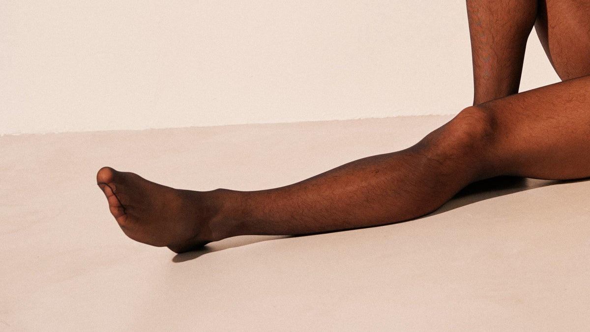 One leg in sheer black tights stretched along a pale floor, the other knee raised behind it