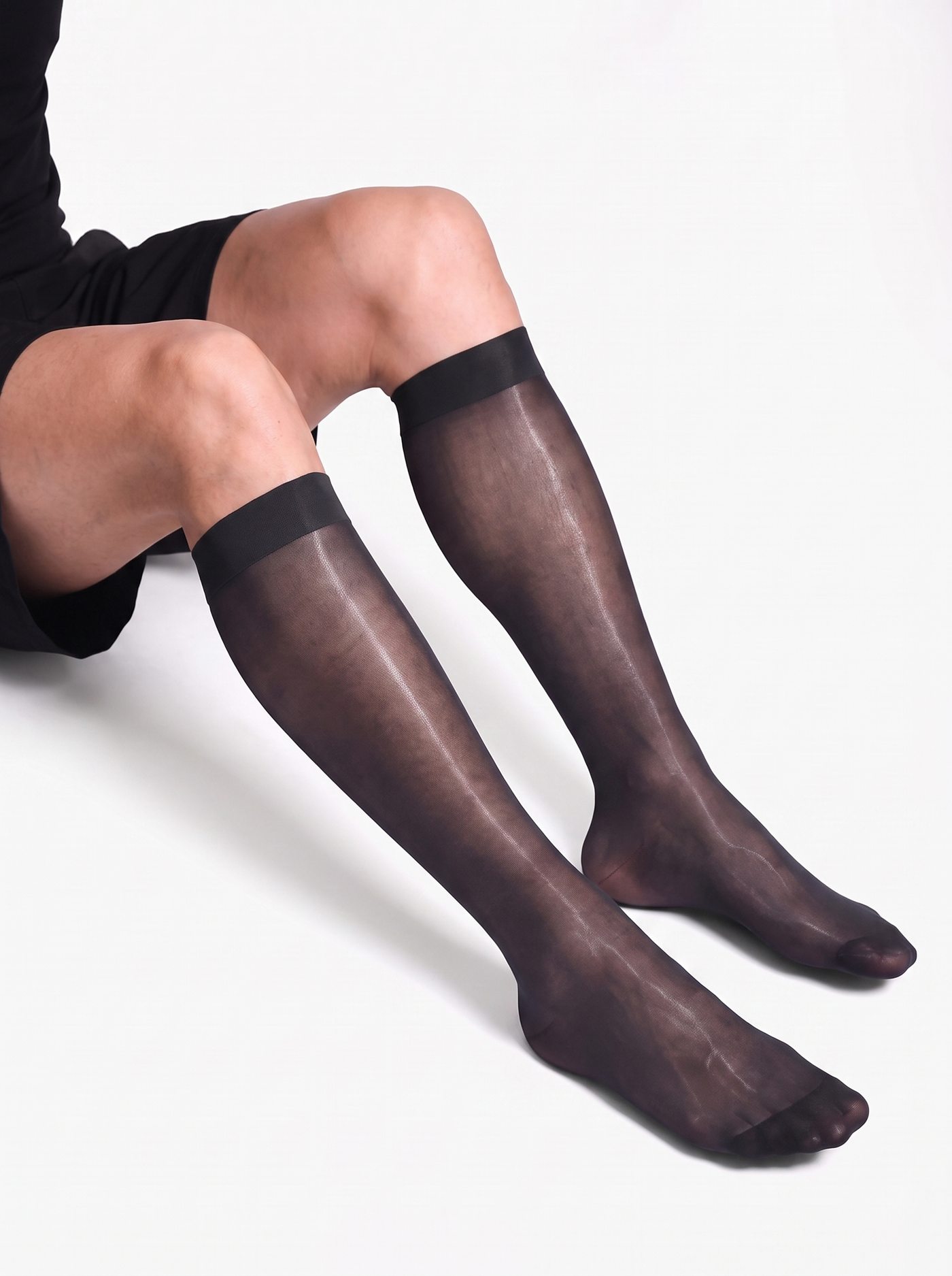 Man seated with knees bent wearing NYLO 10D sheer black dress socks below the knee with solid cuffs