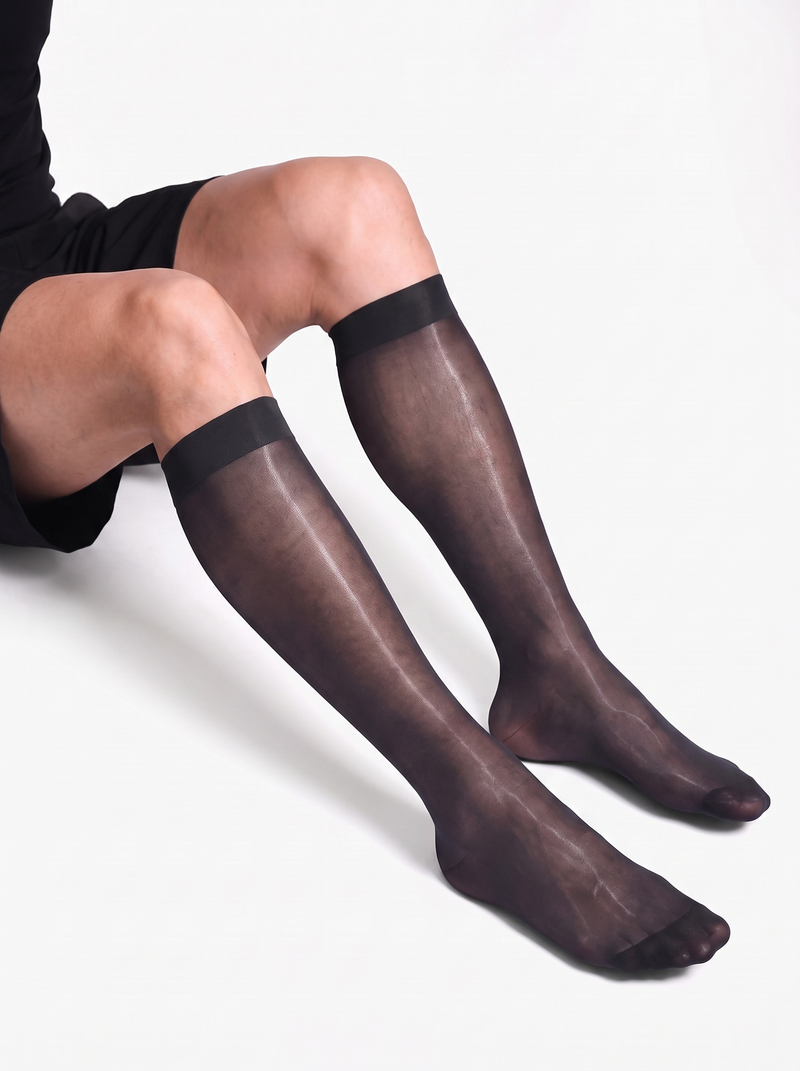 Man seated with knees bent wearing NYLO 10D sheer black dress socks below the knee with solid cuffs