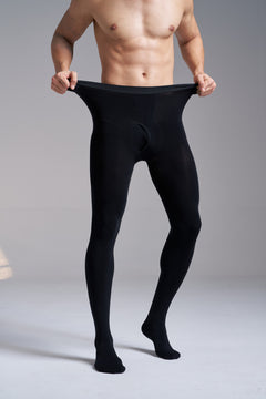 Front view of a man wearing NYLO 120D Opaque Tights in black, pulling the knitted waistband out at both sides, with the underwear-inspired front visible.