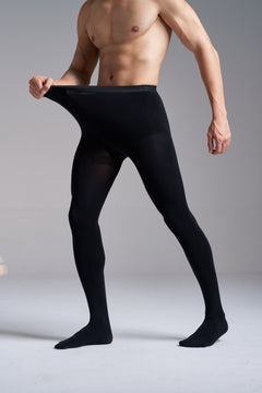 Man wearing NYLO 120D Opaque Tights in black, three quarter view from the shoulders down, stretching the knitted waistband out with one hand.