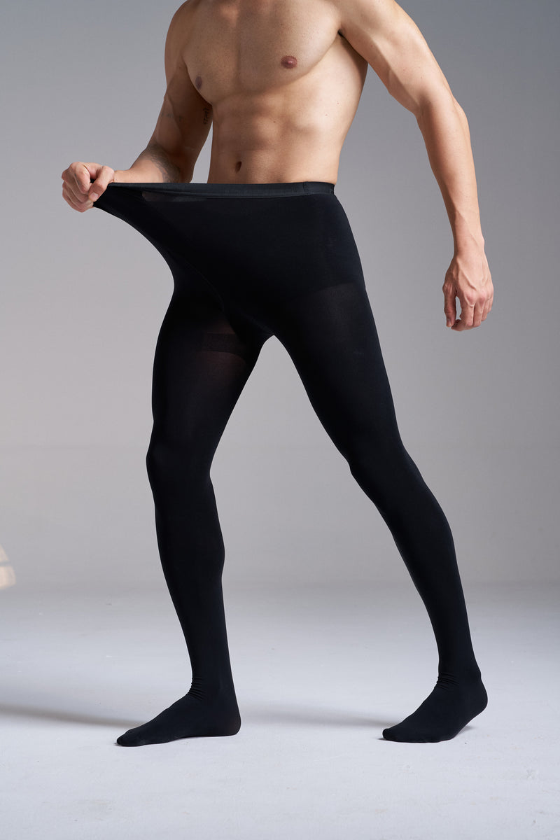 Man wearing NYLO 120D Opaque Tights in black, three quarter view from the shoulders down, stretching the knitted waistband out with one hand.